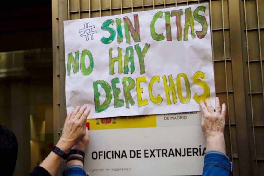 manos enganchando un cartel que dice sin citas no hay derecos en la pared de la oficina de extranjería